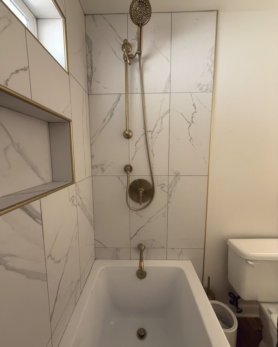 Finished tub and shower with brushed gold fixtures and a tiled niche