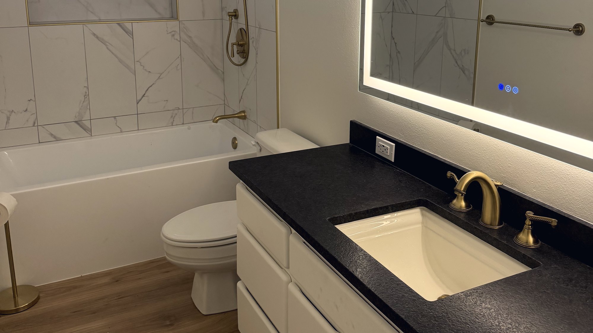 Finished bathroom remodel: black quartz vanity, brushed gold widespread faucet, tub and shower beyond